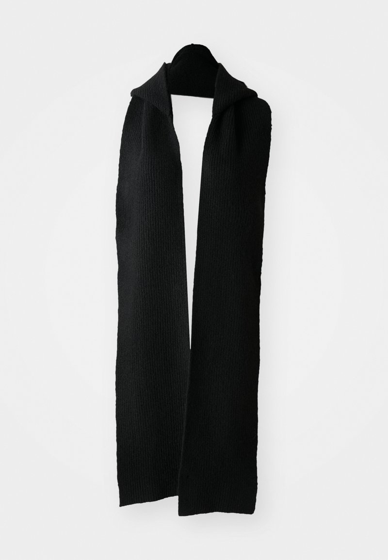 Juodas megztas šalikas, pasižymintis tekstūruotu raštu, ilgos stačiakampės formos ir minkštos medžiagos. Kabo ant kabliuko prieš šviesų foną.
