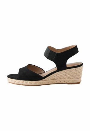 Sandale compensée en daim noir avec une semelle en jute de style espadrille, dotée d'un orteil ouvert et d'une large bride de cheville. Texture lisse et design minimal.