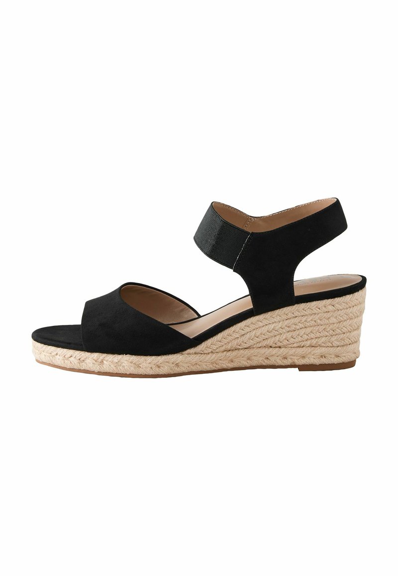 Sandalo wedge in suede nero con suola in juta stile espadrilla, caratterizzato da una punta aperta e una larga cinghia alla caviglia. Texture liscia e design minimal.