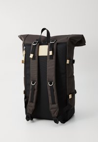 Svart og mørk brun ryggsekk med rullettoppdesign, utstyrt med justerbare stropper, metallbeslag og et minimalistisk lærakcent.