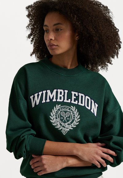 Grønn hettegenser med teksten "WIMBLEDON" i hvitt, har en brodert tennislogo og laurbærdesign. Løs passform, rund hals, teksturert stoff.