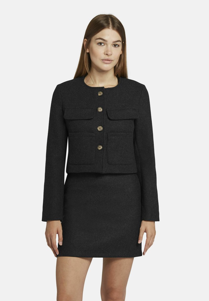 Zwarte cropped jas met twee voorkruiden, knoopsluitingen en lange mouwen, gecombineerd met een bijpassende aansluitende rok. Textuur stof.