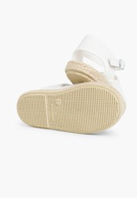 Sandalia de lona blanca con una suela intermedia de yute trenzado, que presenta una suela exterior de goma texturizada y una sola correa ajustable con una hebilla de metal.
