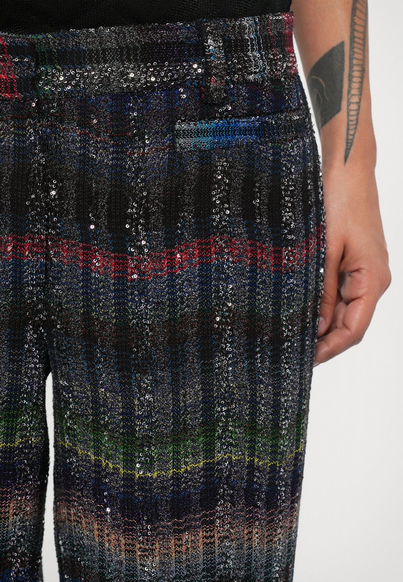 Pantalons à sequins multicolores avec un tissu en tricot texturé. Présente des rayures horizontales de différentes couleurs, un fond noir et une poche latérale.