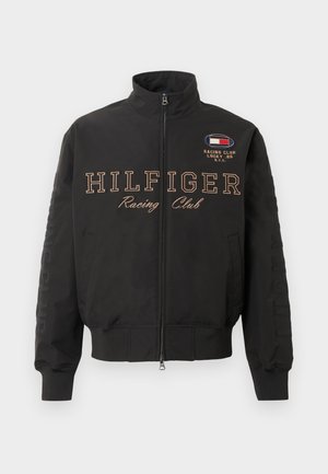 Fekete zipzáras dzseki bordás mandzsettákkal, "HILFIGER Racing Club" felirat az elején, és egy kis verseny embléma a jobb felső mellrészen.
