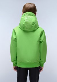 Bambino che indossa una giacca con cappuccio verde brillante con un testo sottile sul cappuccio, visto da dietro su uno sfondo chiaro e semplice.