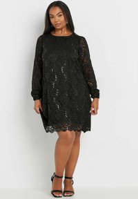 Musta pitsimekko pitkillä hihoilla, kukkakuosi, hammaslaitainen helma ja strassikoristeet. Yhdistetty mustiin naruhattuihin.