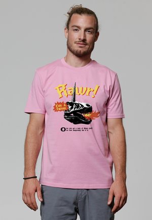 Roze katoenen T-shirt met een afbeelding van een dinosaurus schedel met een eenhoornhoorn, geaccentueerd door speelse gele tekst en een zwarte achtergrond.