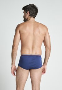 Herrarnas marinblå badshorts med en figursydd design, som har ett mönstrat midjeband och en slät tygtextur. Betraktas från baksidan.