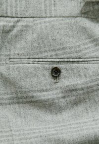 Sivi tekstil sadrži suptilni tkaninski uzorak, stražnji džep s tamnim gumbom i fine detalje šivanja.