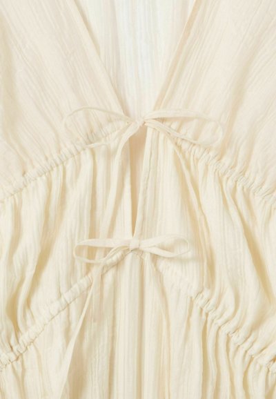 Tessuto color crema stropicciato con due fiocchi annodati e cuciture elastiche raccolte che creano un effetto arricciato.