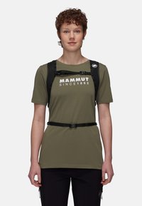 Oliwkowy t-shirt z białym logo, połączony z czarnym uprzężą. Koszulka ma krótkie rękawy i luźny krój, noszona z czarnymi spodniami.
