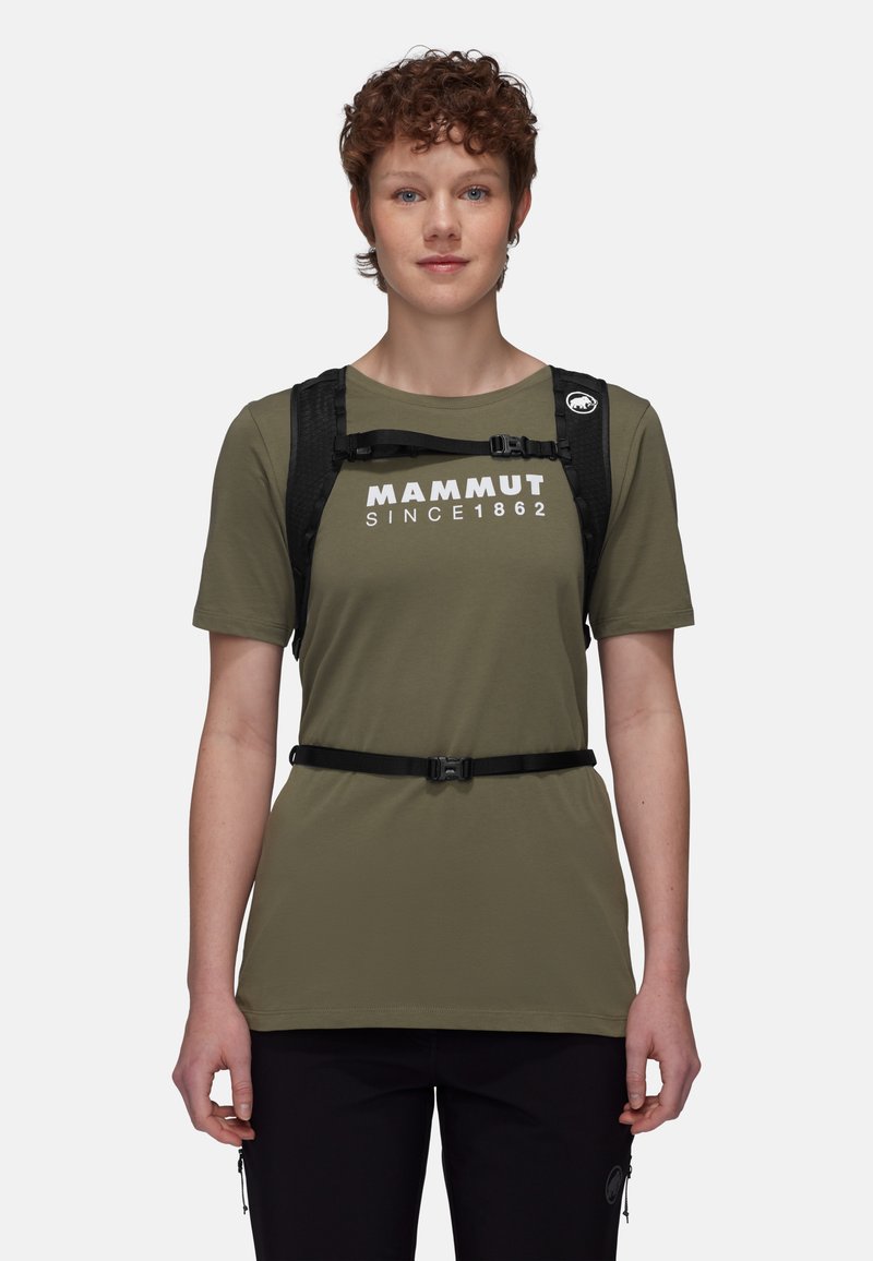 Oliwkowy t-shirt z białym logo, połączony z czarnym uprzężą. Koszulka ma krótkie rękawy i luźny krój, noszona z czarnymi spodniami.