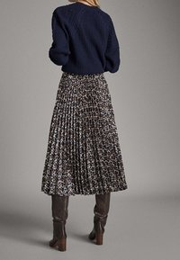 Navy gebreide trui met ribbeltextuur, gecombineerd met een geplooide rok met een bruin en zwarte luipaardprint, aangevuld met bruine kniehoge laarzen.