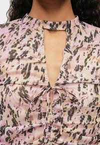 Top w wzór w jasnoróżową i czarną panterę, z dekoltem w kształcie łezki i detalem w postaci wiązania przy szyi, wykonany z miękkiego materiału.