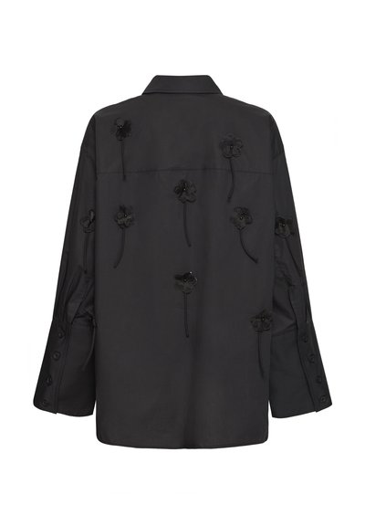 Sort langærmet skjorte med krave, prydet med otte sorte stofblomsterapplikationer med hængende stilke på ryggen og ærmerne.