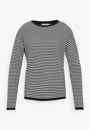 Jersey de manga larga en blanco y negro con un patrón geométrico, cuello redondo y ribetes en negro contrastante a lo largo de los bordes.