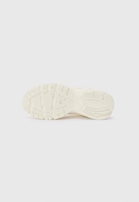 Shoe outsole in light beige with textured treads and grooves, featuring a smooth finish and a curved edge design for traction.