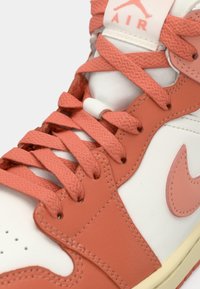 Gros plan sur une basket montante Nike Air orange et blanche avec des lacets orange et le logo Nike swoosh visible sur le côté.