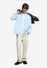 Hele sinine pikade varrukatega särk abstraktse mustriga, valge t-särk all, kriimustatud kreemidest teksad ja mustad paksud jalanõud, rohelise jopet õlal rippumas.