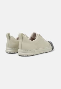 Sneakers in pelle beige chiaro con punta arrotondata, superficie testurizzata, dettagli verde sulla zona del tallone e copertura della punta in gomma di colore più scuro.
