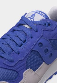 Κοντινό πλάνο του μπλε και γκρι αθλητικού παπουτσιού Saucony με υφασμένα κορδόνια, πλέγμα σε πάνελς και λογότυπο στο πλάι και στη γλώσσα.