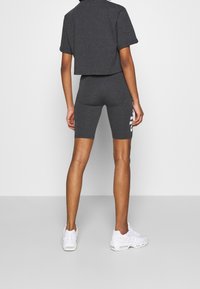 Grå kortärmad t-shirt och matchande högmidjade shorts, båda gjorda av mjukt tyg. Shortsarna har en vit logotyp på sidan. Vita sneakers.