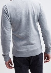 Sudadera de algodón gris con mangas largas y dobladillo acanalado, que presenta un diseño clásico de cuello redondo. Textura suave con un detalle mínimo.