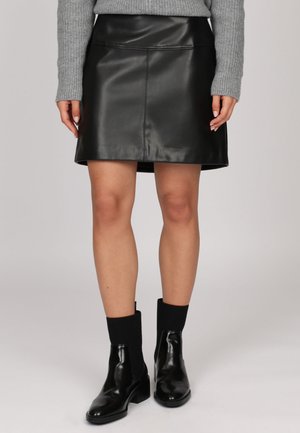 Jupe noire en cuir en forme A avec une texture lisse, dotée d'une couture à la taille. Associée à des bottines noires et un pull gris clair.