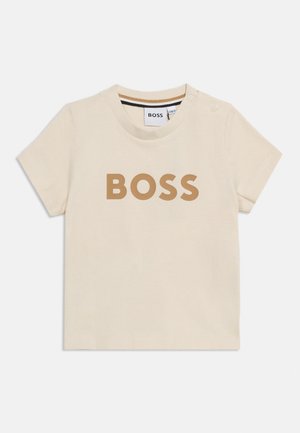 Beige short-sleeve baby T-shirt with "BOSS" printed in brown on front and two snap buttons on left shoulder.