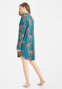 Langsleevige groene jurk met een all-over oranje tijgerprint, met een ontspannen pasvorm en zijsplitten voor gemakkelijke beweging.