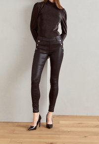 Svarta metalliska tajta byxor med dekorerande knappar på sidorna, kombinerat med en långärmad svart glittrig topp och spetsiga svarta klackar.