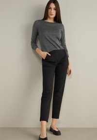 Grå långärmad topp ihopparad med svarta avsmalnande byxor. Outfiten har en slät textur och en minimalistisk design, förhöjd med sidofickor.