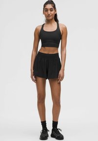 Zwarte sportbeha en shorts met een elastische tailleband en een losse pasvorm. Model draagt zwarte sportieve sneakers en sokken.