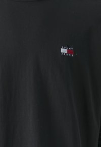 Svart t-skjorte i bomull med en liten rektangulær logo med teksten "TOMMY" og "JEANS" i hvitt og rødt på venstre brystområde.