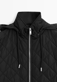 Schwarze steppte Jacke mit hohem Kragen und verstellbare Kapuze, ausgestattet mit einem silbernen Reißverschluss und einem Kordelzug mit silbernen Hardware-Akzenten.