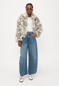 Faux fur-jakke i beige med brune flekker, hvit ribbet topp, vide lyseblå jeans og hvite sko med flere stropper.