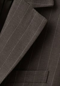 Temno sivo suknjič s tankimi belimi vertikalnimi črtami, ki so vidne na tkanini, ovratnik in prsni žep.