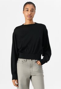Black cropped sweatshirt with long sleeves and elastic hem, paired with light gray fitted jeans. Smooth texture, relaxed design.