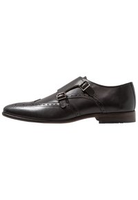 Svart läderskor med dubbla spännen, spetsig tå, dekorativ broguedetaljering och en platt träklack. Slät textur och elegant design.