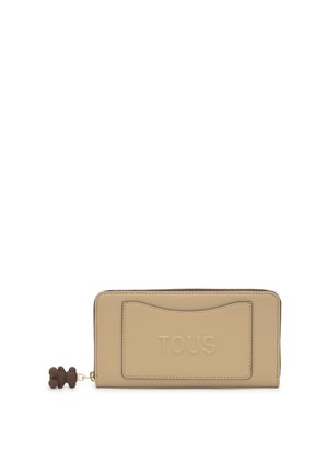 Cartera de cuero beige con cremallera, logo "TOUS" en relieve, ranura para tarjetas en el frente y tirador de cremallera con osito de peluche marrón.