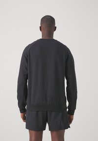 Sweatshirt noir en matière douce, avec un col ras du cou, des manches raglan et un ourlet côtelé. La vue arrière montre un design lisse et minimaliste.
