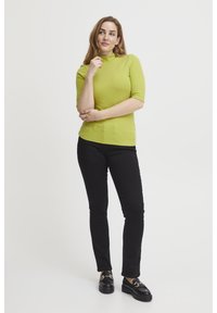 Limegrön ribbad topp med hög krage och korta ärmar, i kombination med svarta smala byxor och svarta chunky loafers.