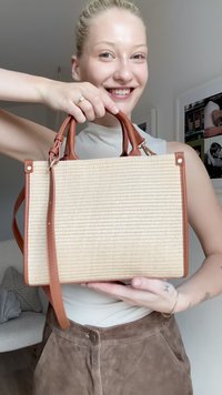 Woven straw handbag with brown leather handles and accents. Rectangular shape, textured surface, and detachable shoulder strap.