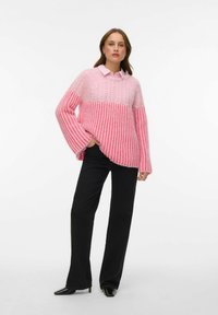 Roosa kootud kampsun tekstuurse mustriga, millel on laiad varrukad ja ülaosas helekollane varjund. Sobitatud mustade pükstega.