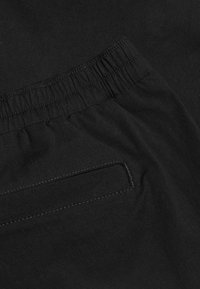 Czarny materiał z elastycznym pasem i poziomą kieszenią na suwak z widocznym przeszyciem na miękkim materiale.