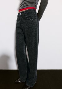 Jeans iz temno sivo, z leopardjim potiskom in sproščenim krojem. Značilnosti vključujejo rdeč pas, sprednje žepke in dekorativne srebrne žeblje.