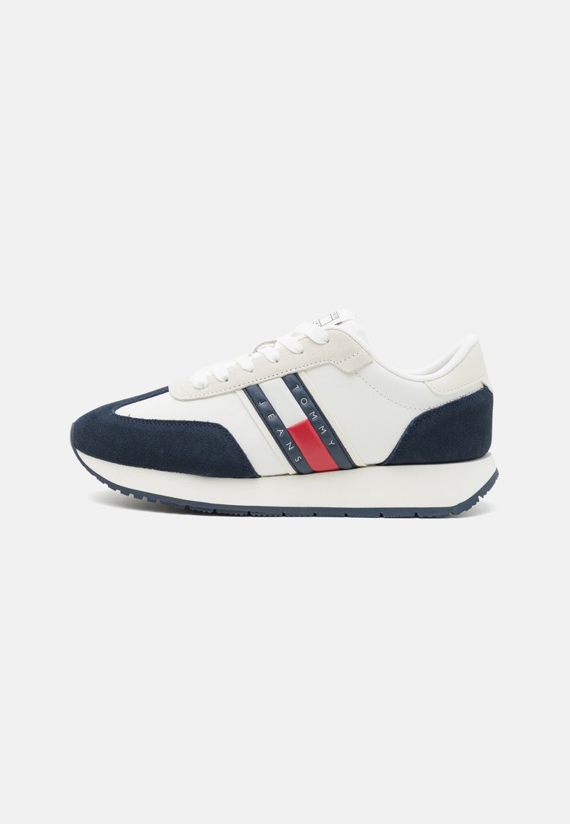 Sneaker aus einer Kombination von weißem Leder und navyfarbenem Wildleder, mit blauen und roten horizontalen Streifen an der Seite und einer Gummisohle.