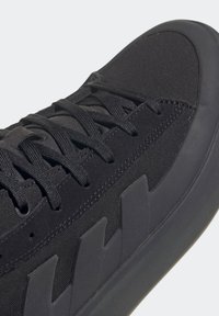 Černá atletická bota s texturovaným svrškem z látky, plochými tkaničkami a gumovou podrážkou. Disponuje výraznými černými akcenty na boční straně a hladkými okraji.