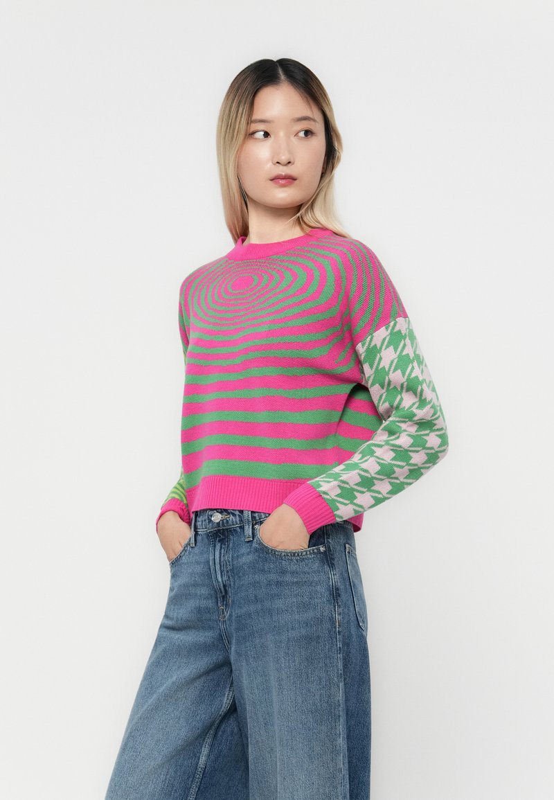 Sweter dziany z na przemian występującymi różowymi i zielonymi spiralnymi paskami na korpusie, z wzorem w pepitkę na rękawach.
